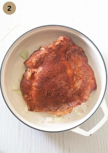 seasoned skinless turkey thigh sitting on chopped onions in a large dutch oven.