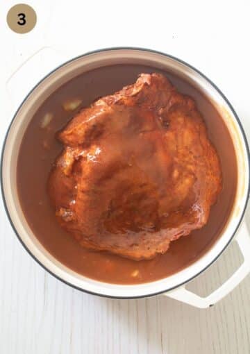 skinless turkey thigh covered with sauce before cooking it in a dutch oven.