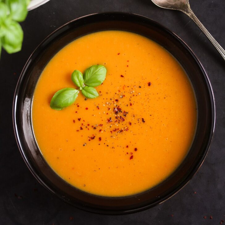 sweet potato carrot ginger soup garnished with basil in a black bowl.