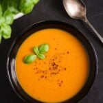 bowl of sweet potato soup on a black background with basil.