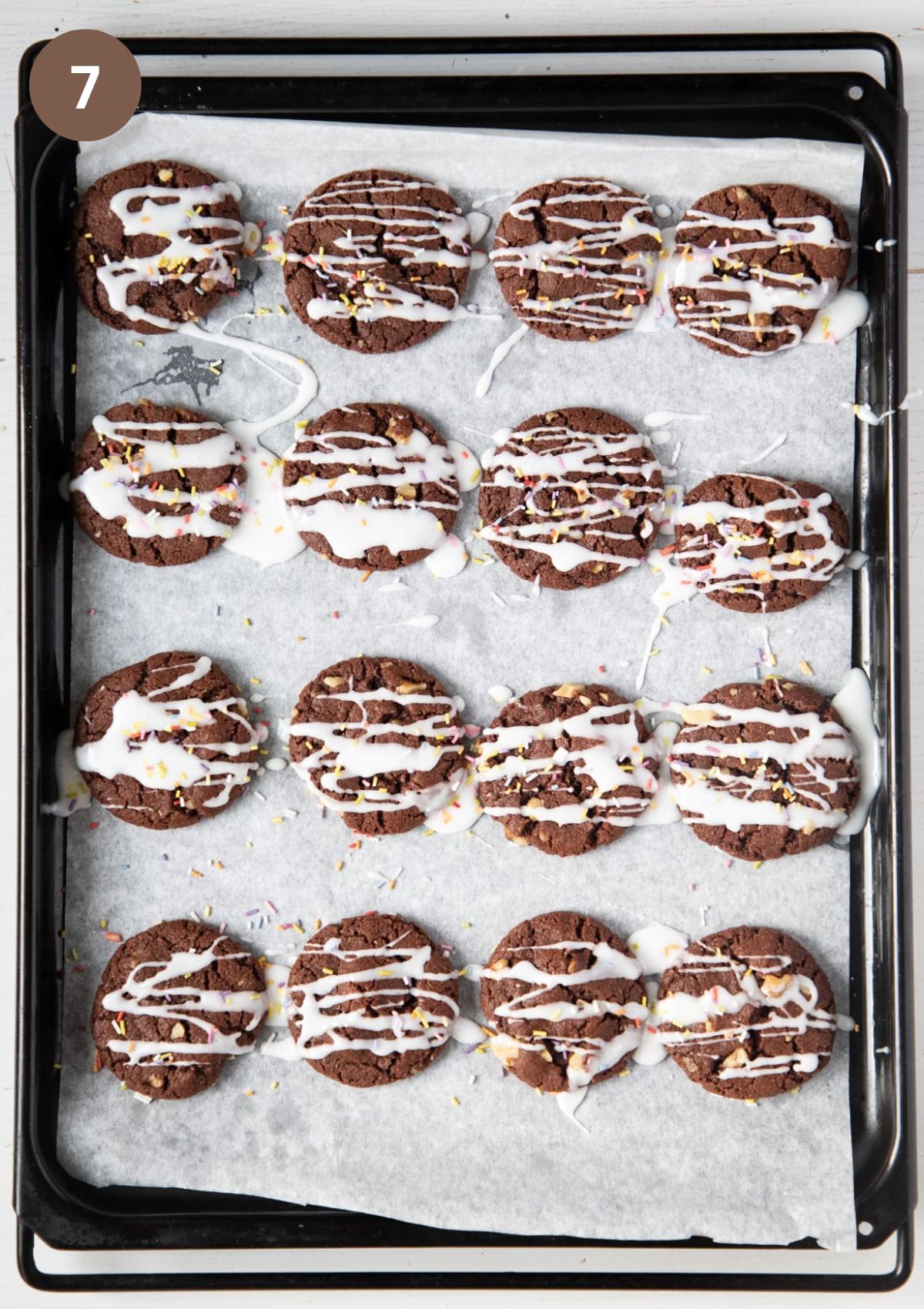 many cookies on a baking sheet drizzled with glaze and sprinkled with sprinkles.