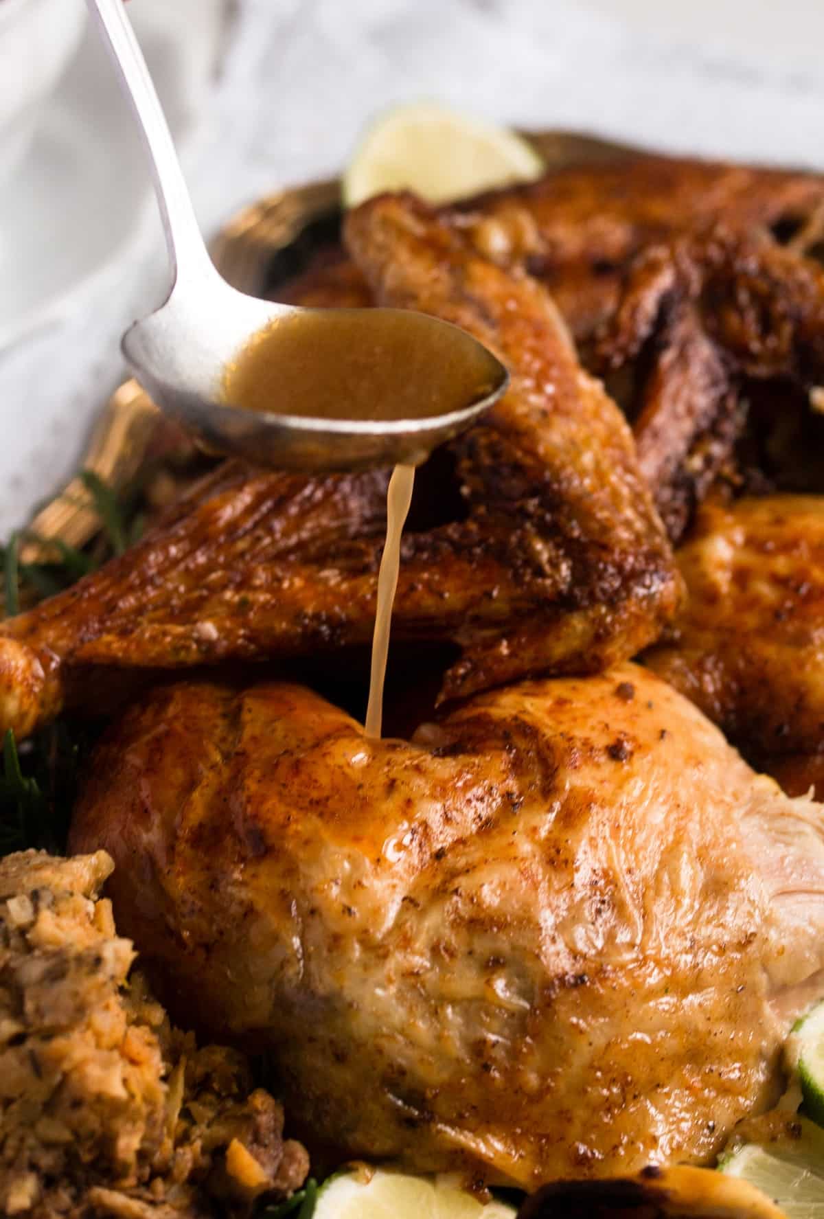 pouring gravy with a spoon on carved roasted chicken pieces.
