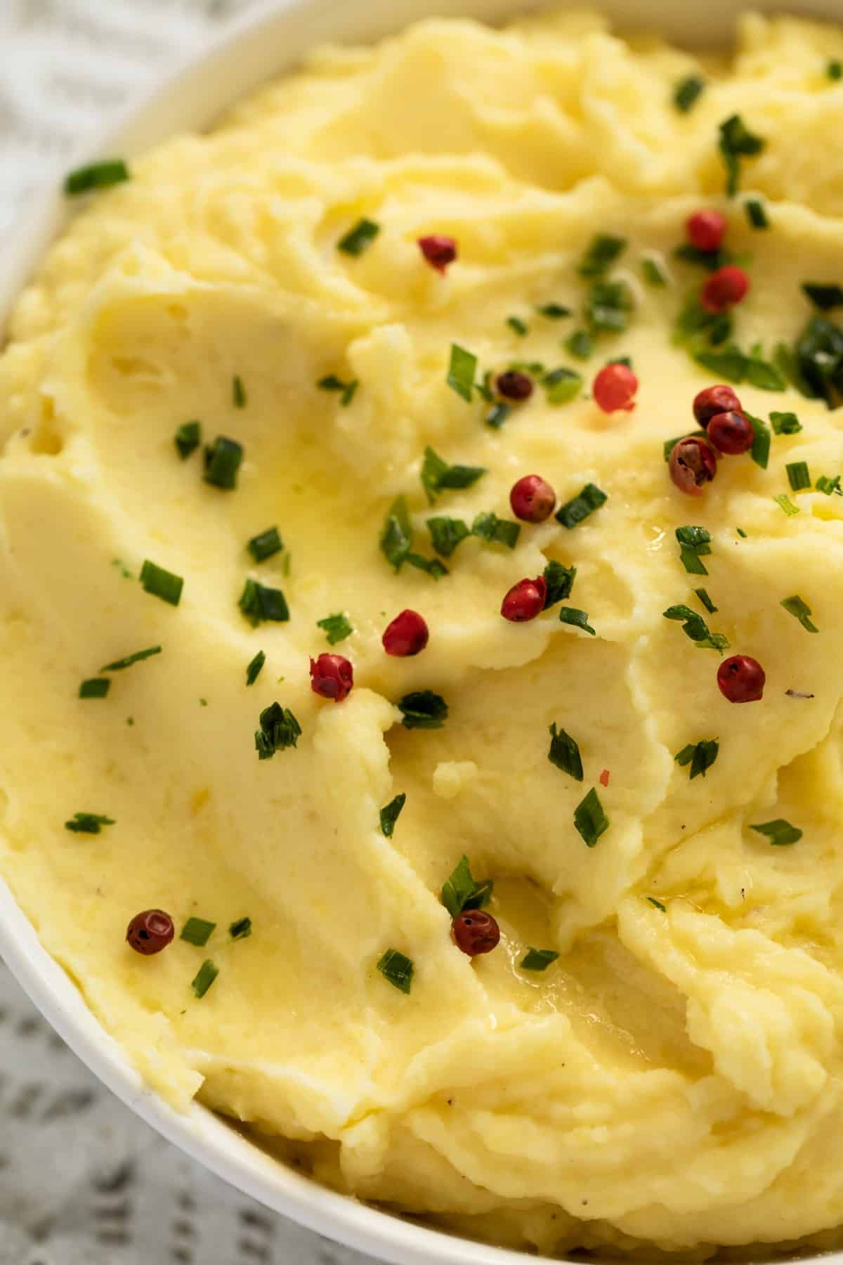 close up bowl of potato mash sprinkled with red peppercorns and parsley.