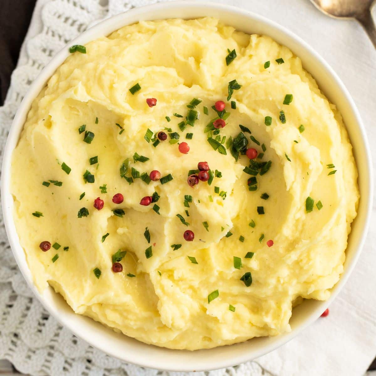 overhead view of a bowl of truffle mashed potatoes sprinkled with parsley and red pepperberries.