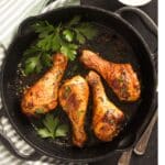 cast iron chicken drumsticks with parsley around it.