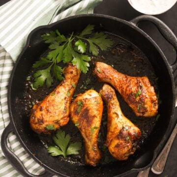 overhead view of a cast iron skillet with four chicken legs and fresh parsley inside it.