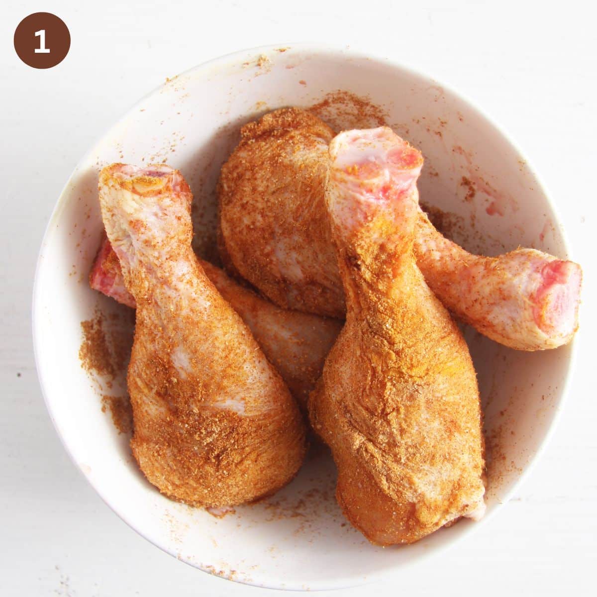 raw chicken legs coated with spices in a bowl.