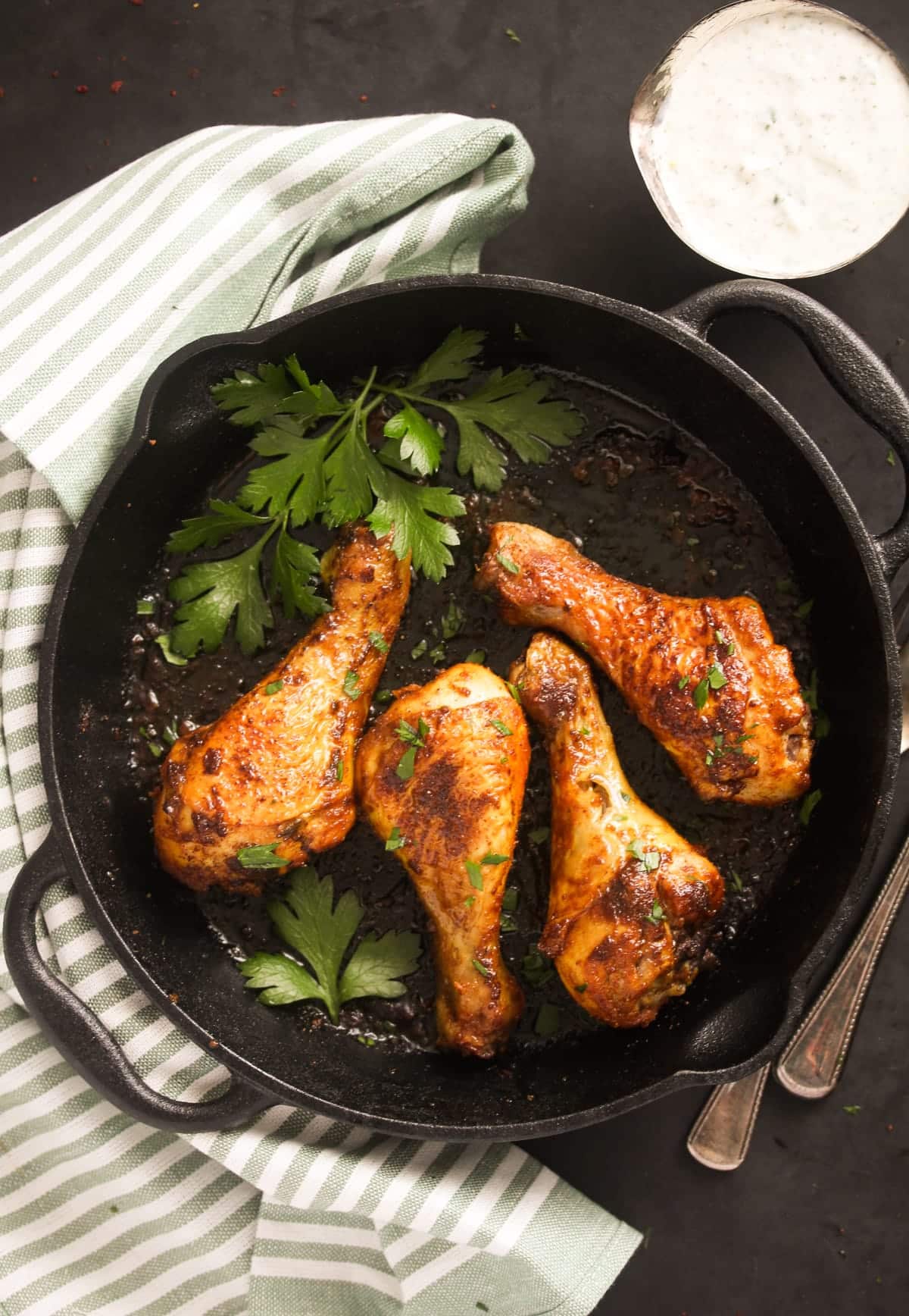 overhead view of a cast iron skillet with four chicken legs and fresh parsley inside it.