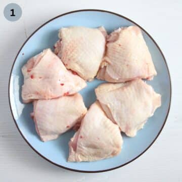 six raw thighs on a pale blue plate.