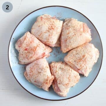 six raw and seasoned skin on chicken thighs on a blue plate.