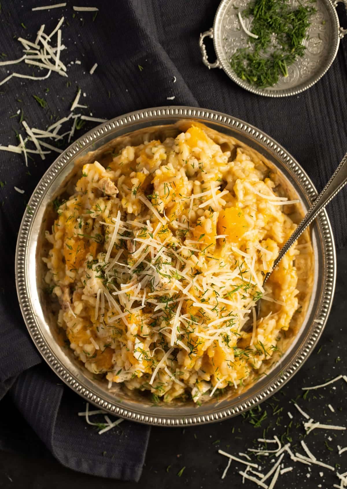 overhead view of a silver plate with risotto on a black cloth with herbs beside it.