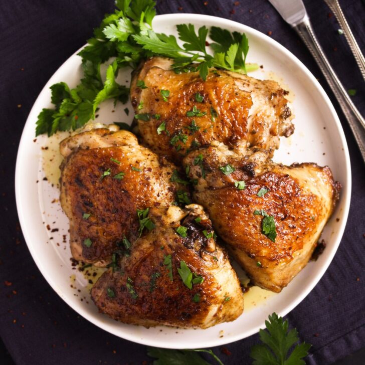 plate with four pan-fried chicken thighs and parsley.