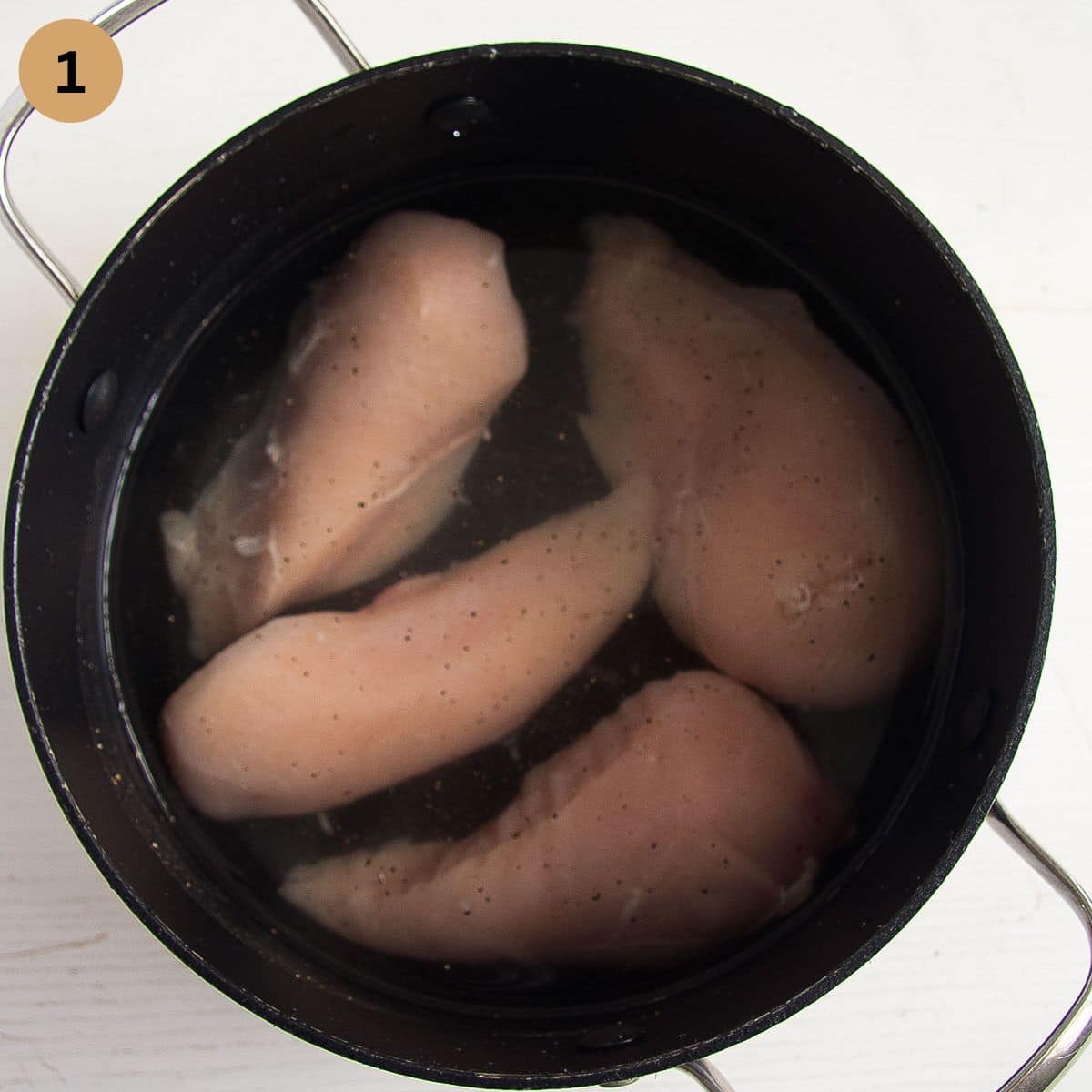 four raw chicken breasts covered with water in a small pan.