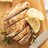 sliced cooked chicken cooked from frozen on a cutting board with a knife and lemon.