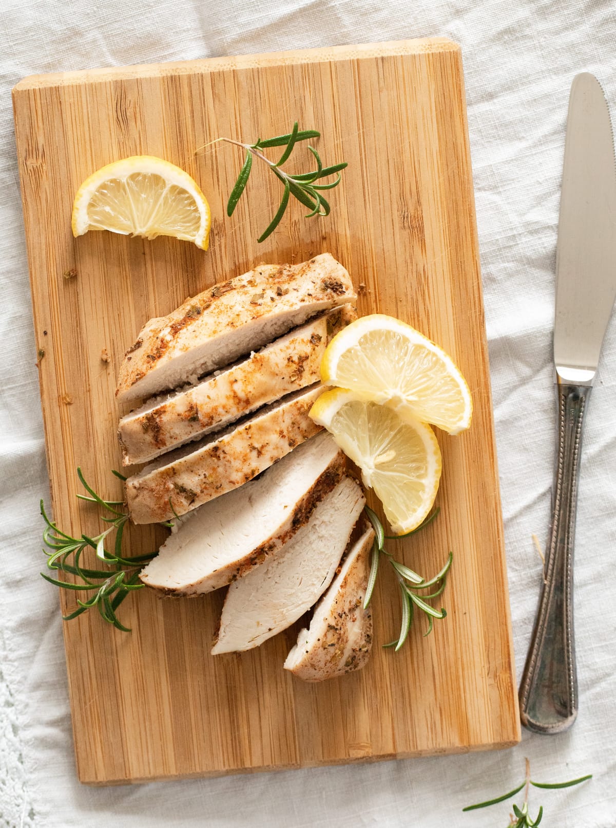 overhead image of a sliced piece of chicken on a cutting board, a knife beside it.