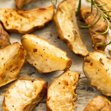 many sliced sunchokes and a sprig of rosemary on a baking sheet.