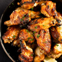 black bowl full of hot wings with lemon wedges.