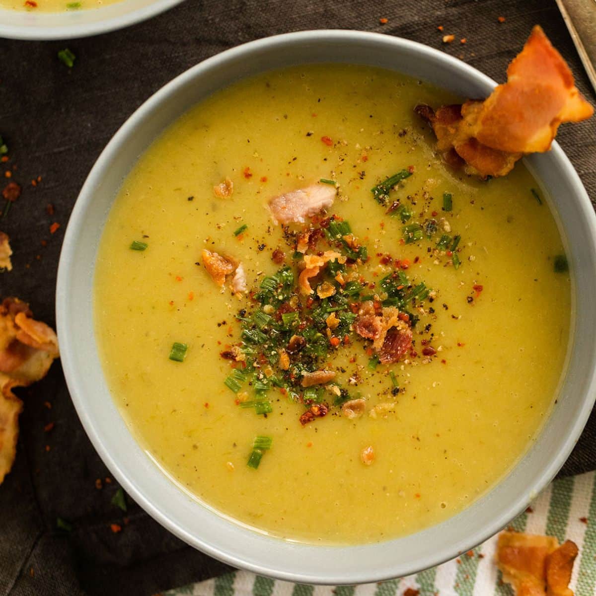 creamy bacon leek and potato soup topped with crispy bacon and chives in a bowl.