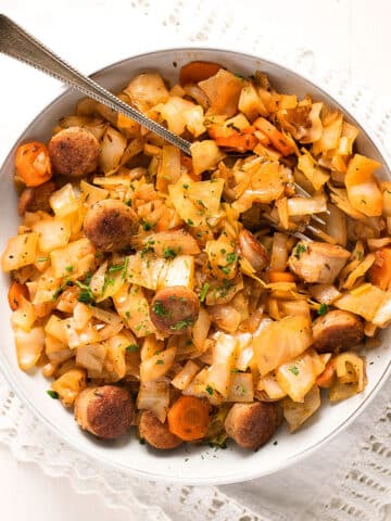 bowl with fried cabbage with sausage with a fork sticking in the food.