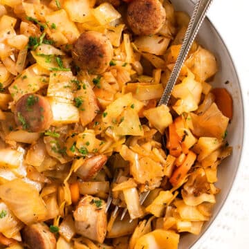 bowl with fried cabbage and sausages sprinkled with parsley.