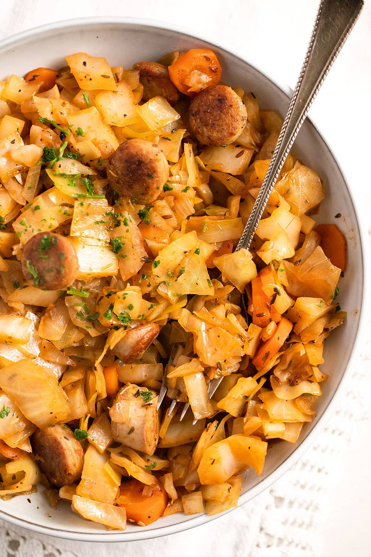 bowl with fried cabbage and sausages sprinkled with parsley.