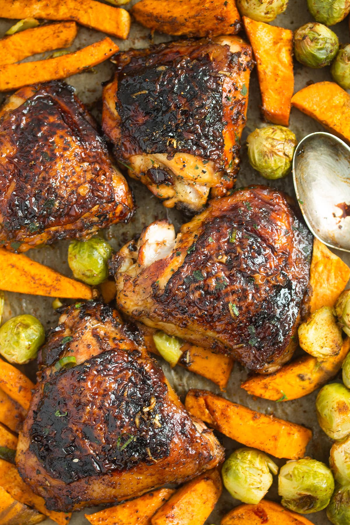 four chicken thighs roasted with sweet potatoes and brussels sprouts.