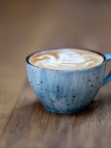 small blue cup with coffee on a brown board.