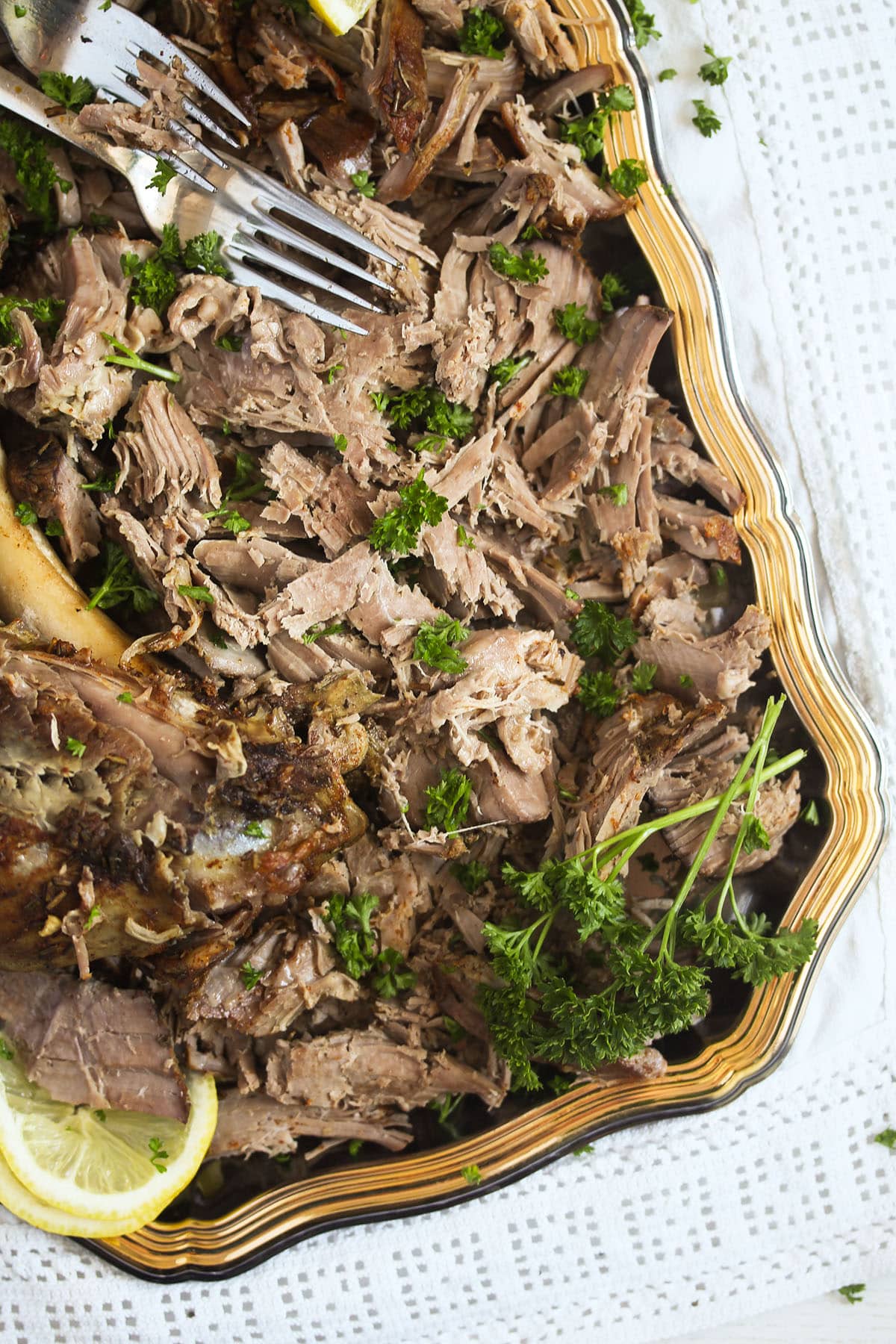 platter with pulled lamb, parsley, lemon and a fork.