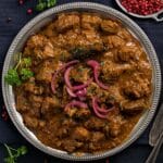 slow cooker lamb curry topped with red onions on a silver plate.