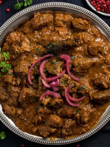 slow cooker lamb curry topped with red onions on a silver plate.