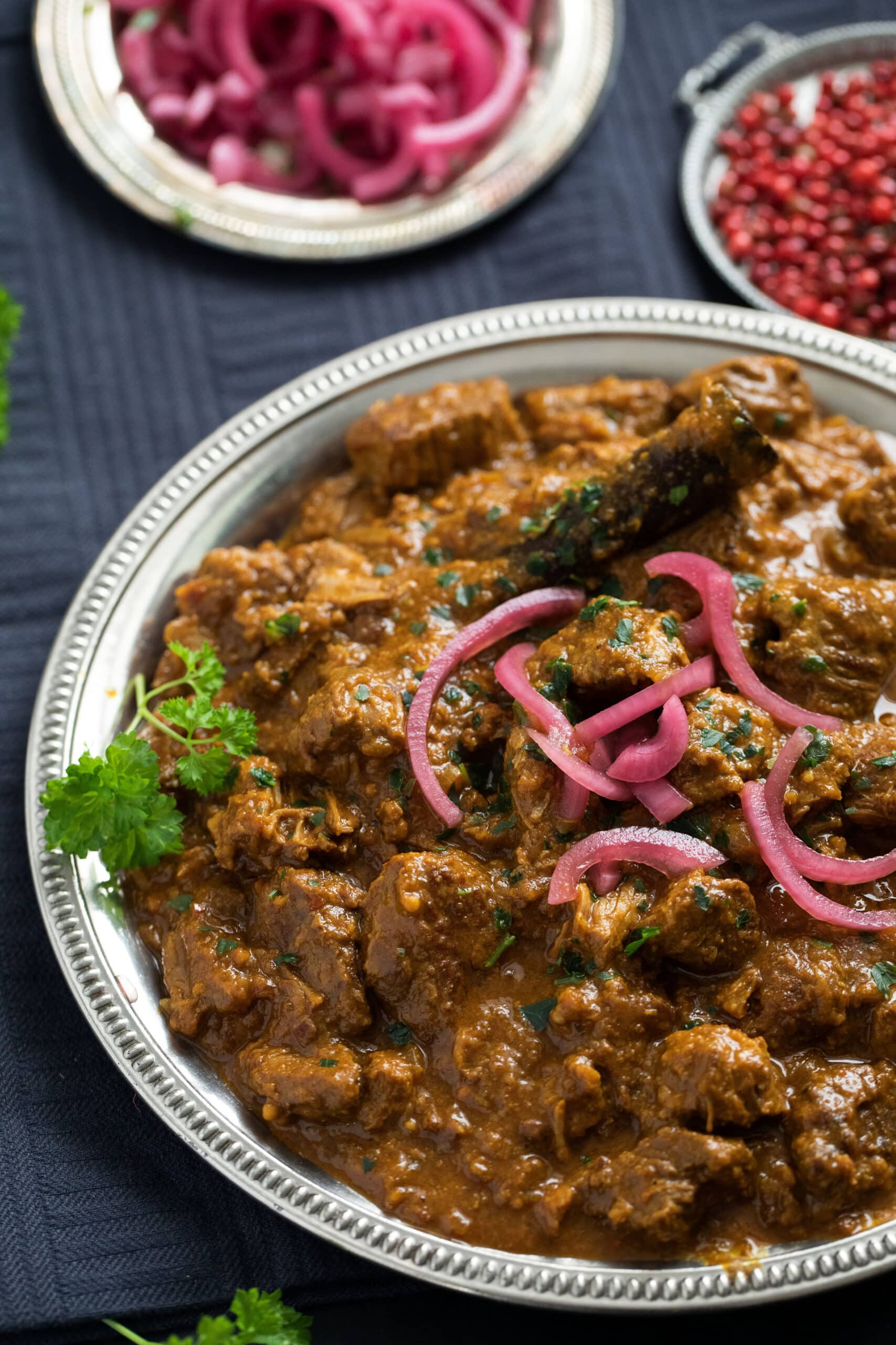 plate with lamb curry and smaller plates with pickled onions and red peppercorns.