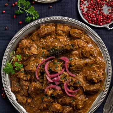 plate of curry with lamb and coconut milk, served with pickled onions and red peppercorns.