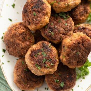 many brown ground veal meatballs with parsley on a plate.