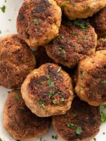 many brown ground veal meatballs with parsley on a plate.