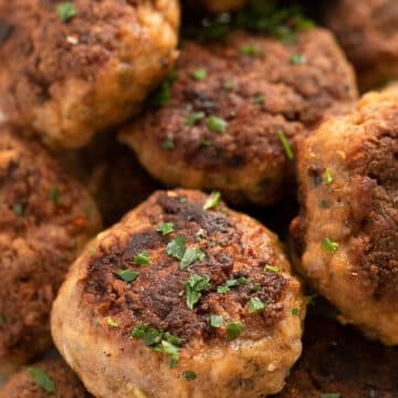 close up deeply brown calf meatballs sprinkled with parsley.