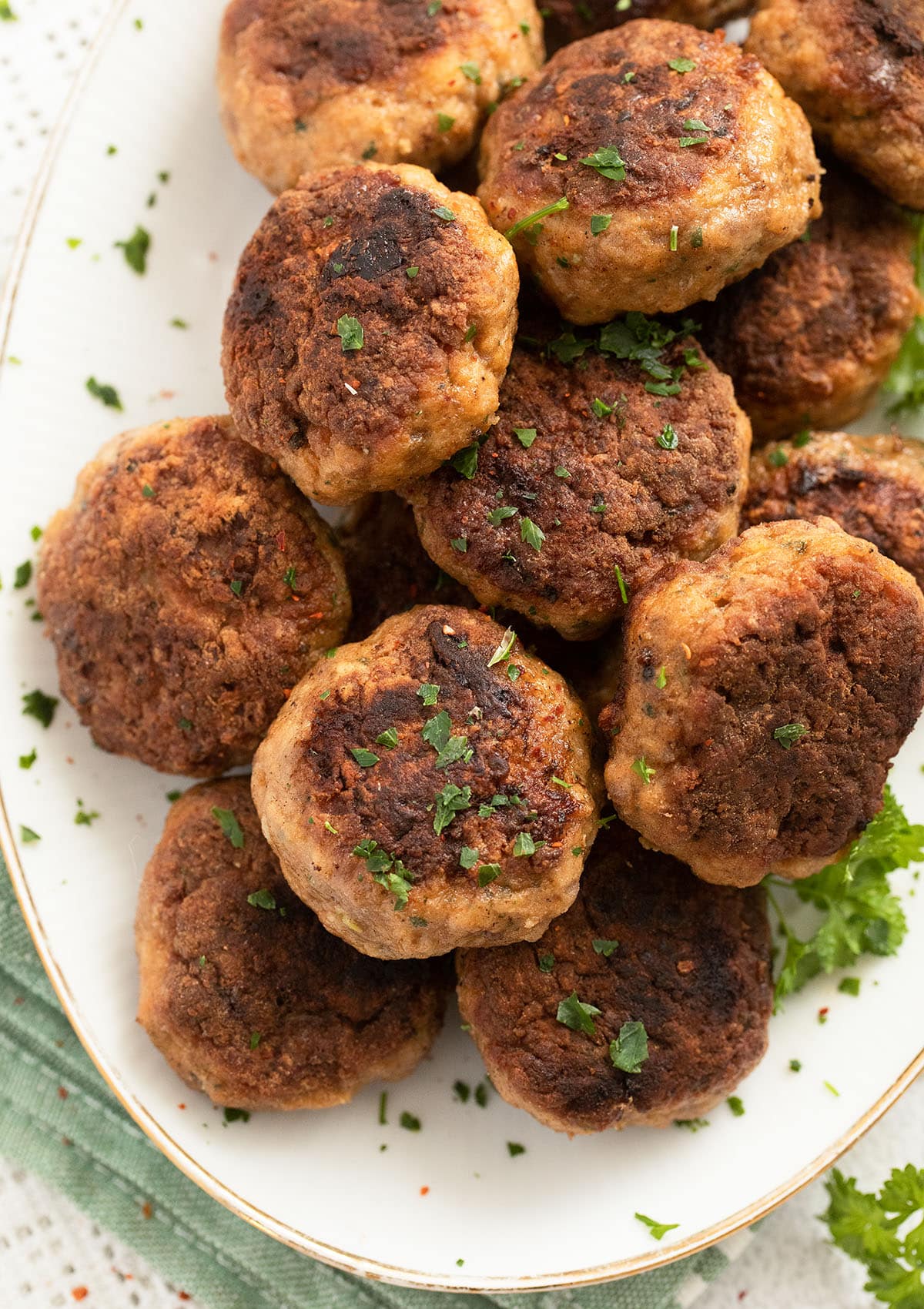many meatballs with ground veal and parsley on a white platter.