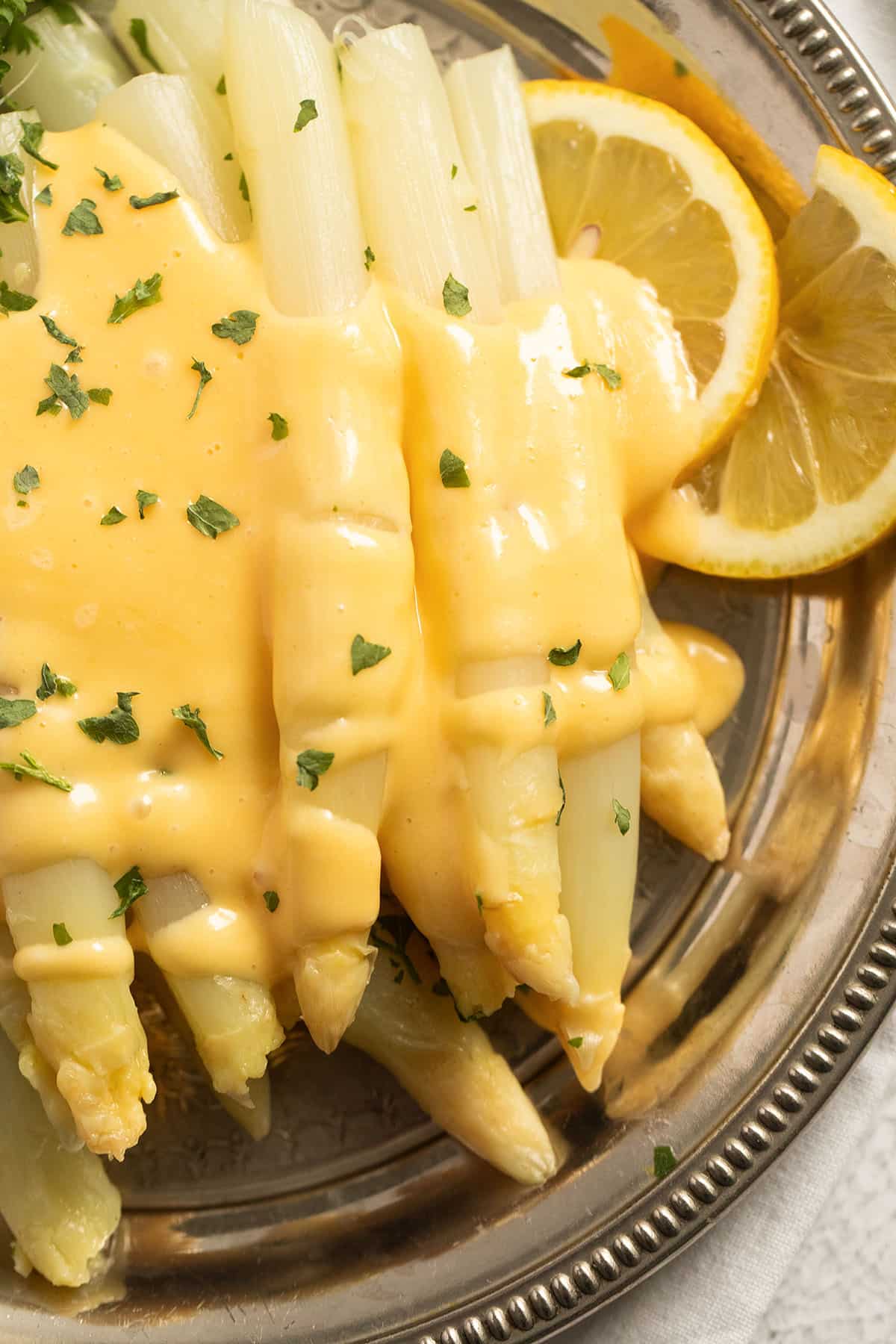 german white asparagus covered with sauce hollandaise and sprinkled with parsley.