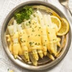 german white asparagus with white sauce and lemon wedges on a round platter.
