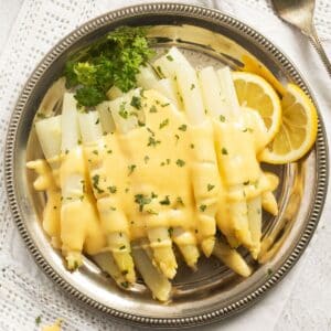 german white asparagus with white sauce and lemon wedges on a round platter.