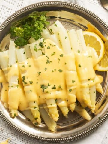 german white asparagus with white sauce and lemon wedges on a round platter.