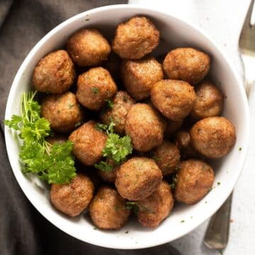 bowl with many golden brown air fryer frozen meatballs with parsley on the side.