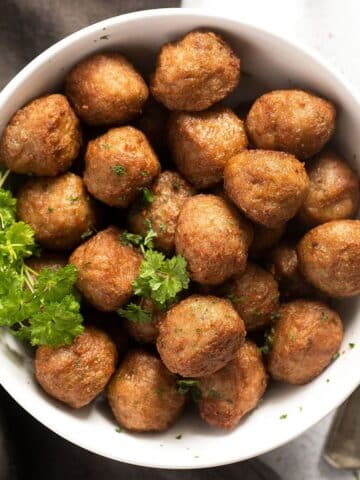 bowl with many golden brown air fryer frozen meatballs with parsley on the side.
