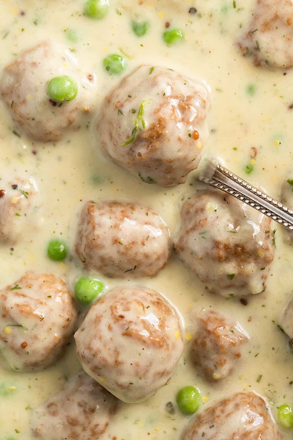 meatballs in swedish sauce with peas, a spoon lifting one meatball.