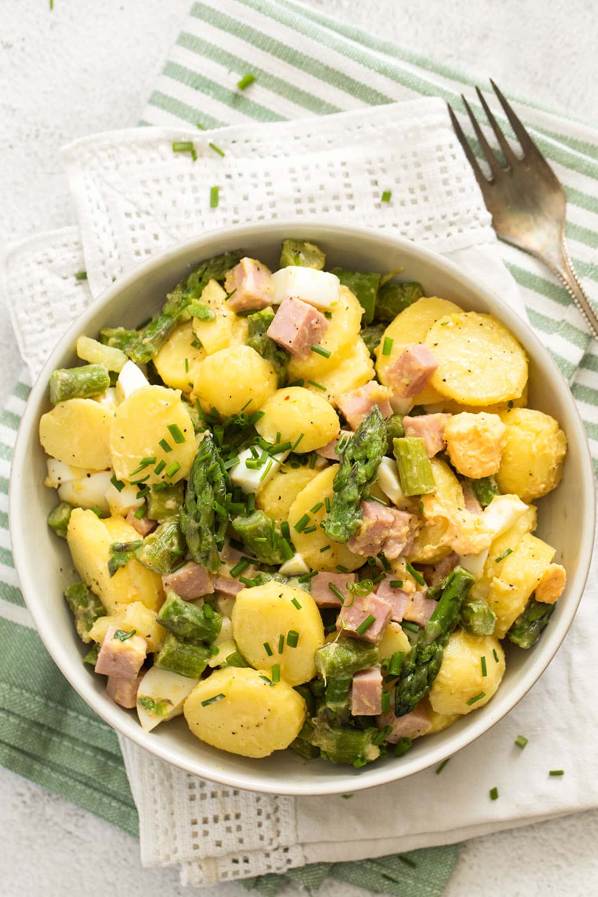 overhead view of a bowl of potato salad with asparagus and ham.