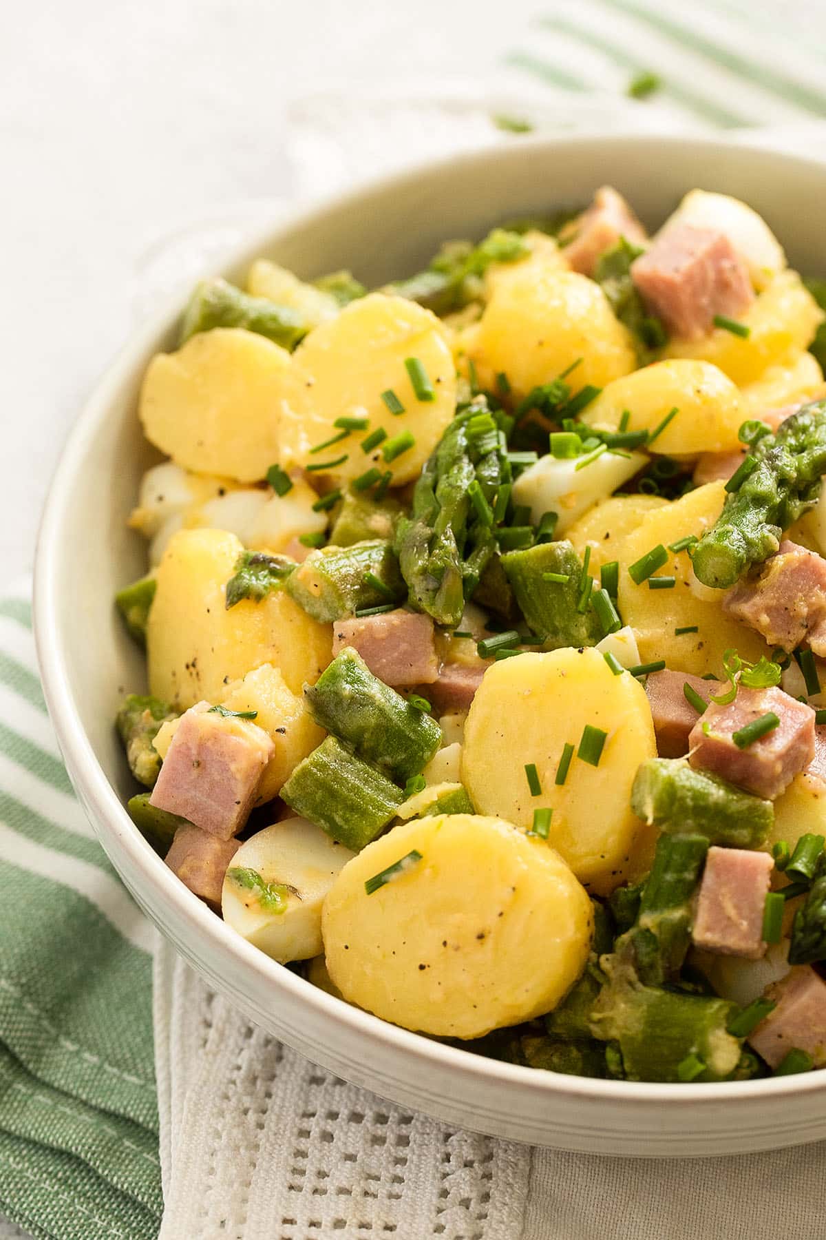 close up bowl of cold salad with asparagus, potatoes, ham, and eggs.