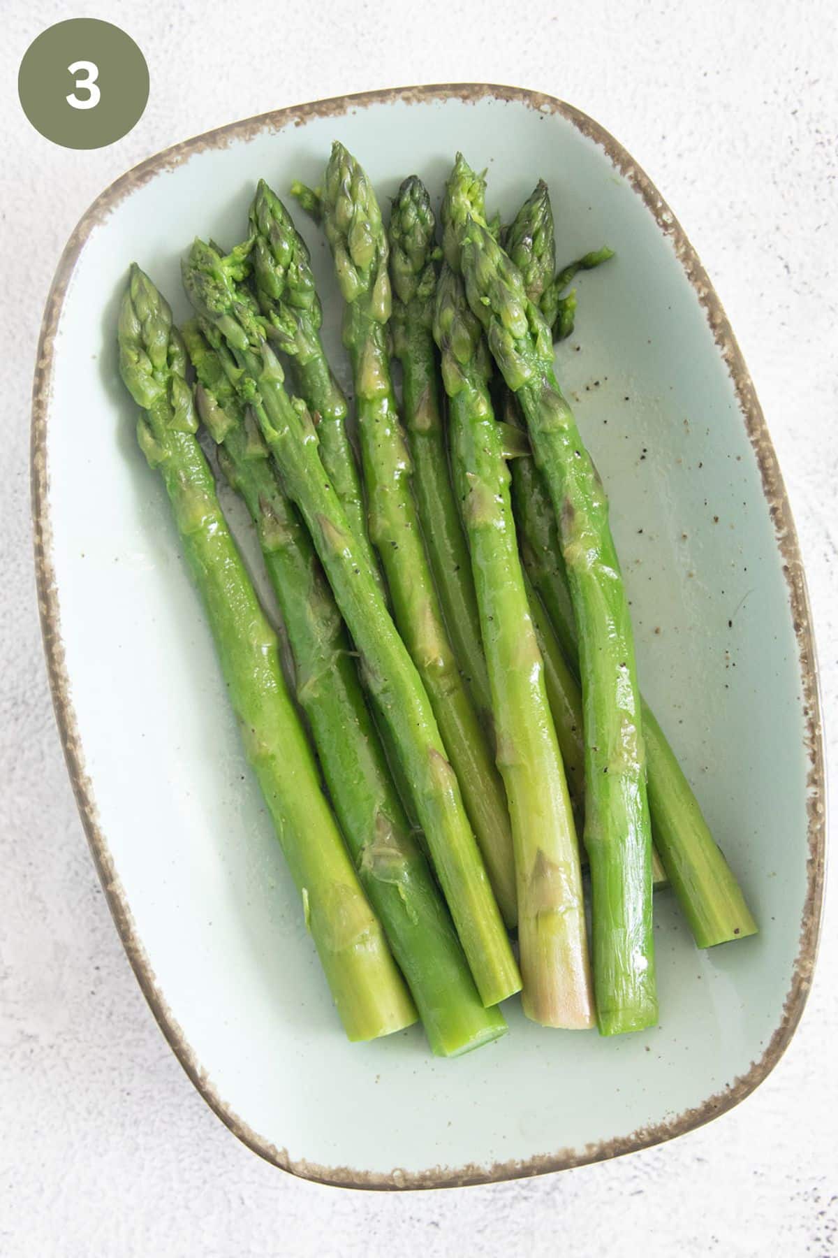 green asparagus spear marinating on a light blue platter.