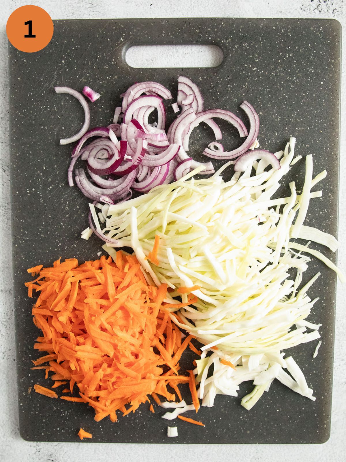 shredded white cabbage, carrots and onions for making slaw on a cutting gray cutting board.