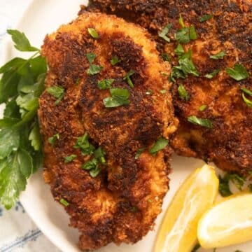 close up of a crispy chicken fillet served with parsley and lemon wedges.