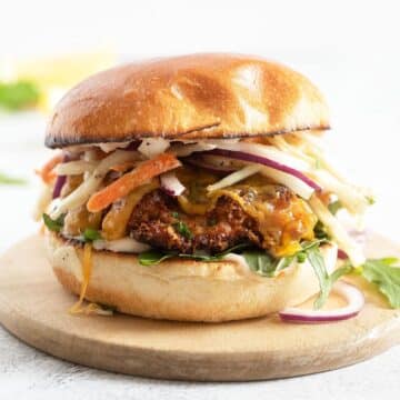 crispy chicken fillet burger with coleslaw on a round wooden board.