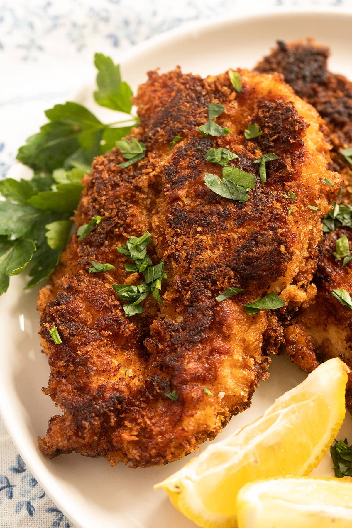 close up of one large crispy chicken fillet served with parsley and lemon wedges.